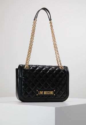 Sac à main en cuir matelassé noir avec des lanières en chaîne dorée et une plaque logo dorée "LOVE MOSCHINO" à l'avant, exposé sur un piédestal blanc.