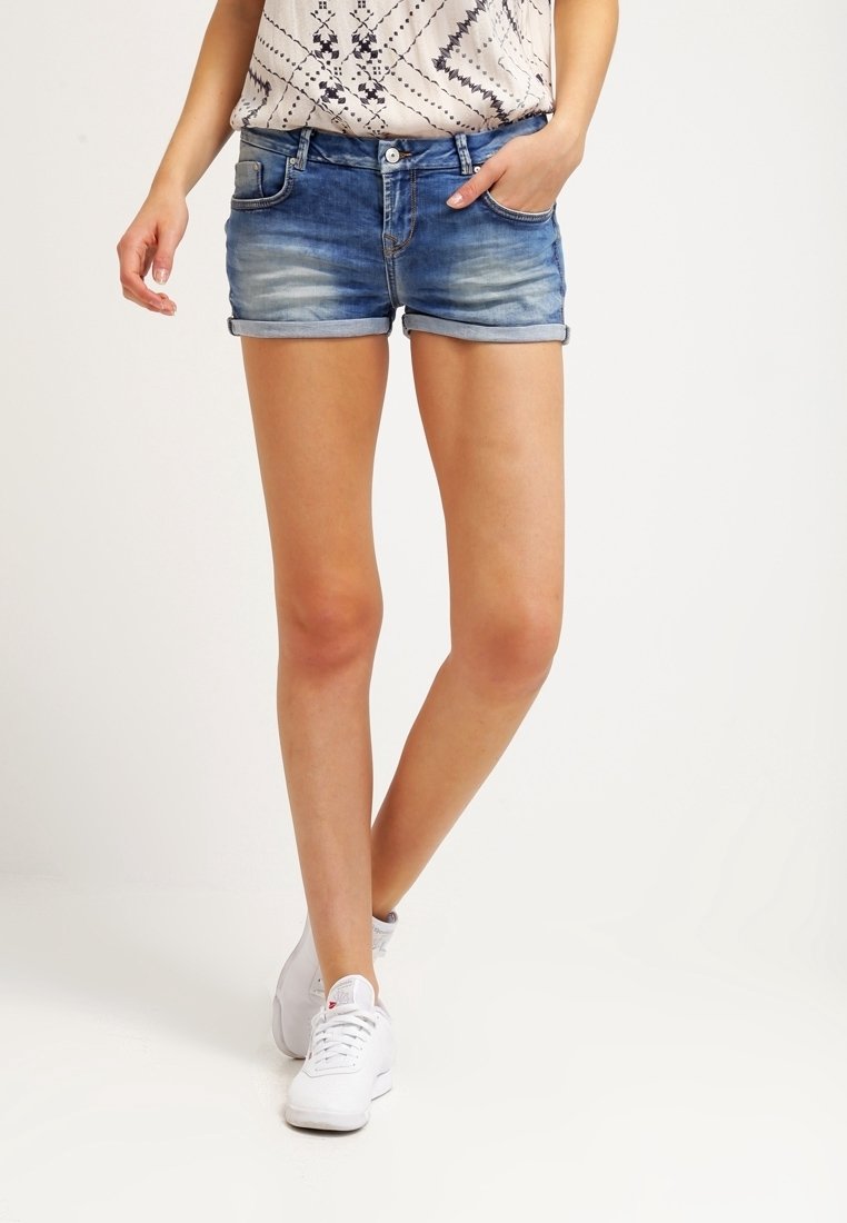 Světle modré džínové šortky s vybledlou texturou, ohrnutými lemy a pěti kapsami, v kombinaci s vzorovaným topem a bílými teniskami.