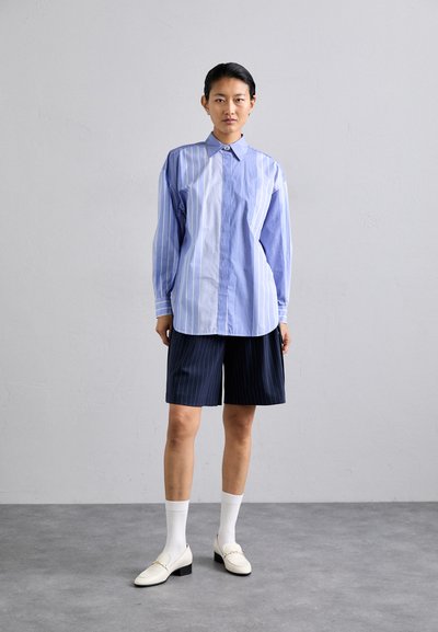 Lys blå og hvid stribet oversized skjorte med krave, parret med marineblå pinstripe shorts, hvide sokker og hvide hæle loafers.