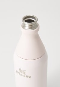 Botella de agua de acero inoxidable en rosa suave con un acabado mate, diseño cónico y un borde plateado en la abertura; presenta un logotipo.