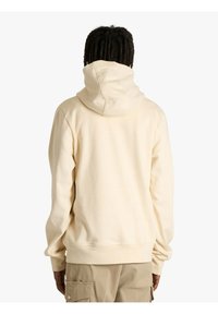 Felpa con cappuccio color crema con cappuccio grande e regolabile, polsini a coste e banda in vita. Tessuto morbido e strutturato. Vista posteriore che mostra la semplicità del design.