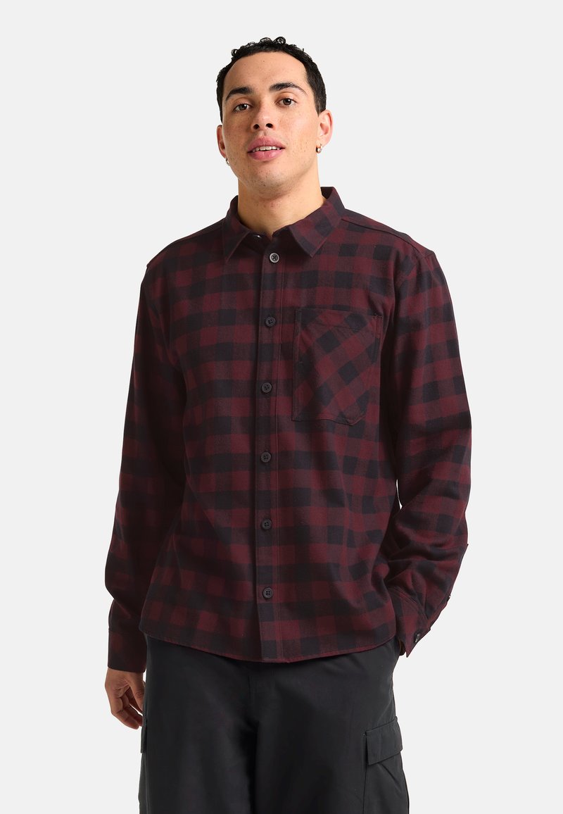 Chemise en flanelle à carreaux dans des tons de rouge foncé et noir, avec un devant à bouton, un col, des manches longues et une poche poitrine. Texture douce.