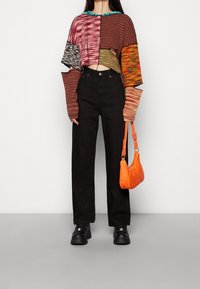 Crop top w stylu szydełkowym o mieszanych kolorach i fakturach, w połączeniu z czarnymi jeansami z wysokim stanem i pomarańczową torebką. Czarne masywne buty.