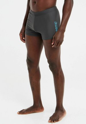 Graue Badehose aus glattem, dehnbarem Material, mit einem türkisfarbenen Logo auf der linken Seite und einem Schnitt bis zur Mitte des Oberschenkels.