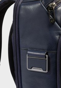 Mochila de cuero azul oscuro con acabado texturizado, con un logo de herrajes plateados, cierre de cremallera y costuras detalladas.