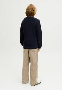 Dunkelblauer Strickpullover mit Rundhalsausschnitt, langen Ärmeln und gerippten Bündchen, kombiniert mit beigen weiten Hosen und schwarzen Schuhen.