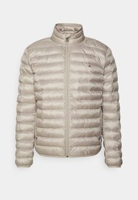 Giubbotto imbottito beige con collo alto, chiusura con zip e cuciture orizzontali. Presenta tasche laterali e un piccolo logo sul petto.