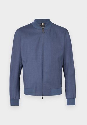 Námořnicky modrá bomber bunda se zipem vpředu, žebrovanými manžetami a límcem. Vyrobena z hladké látky s jemnou texturou. Dvě boční kapsy.