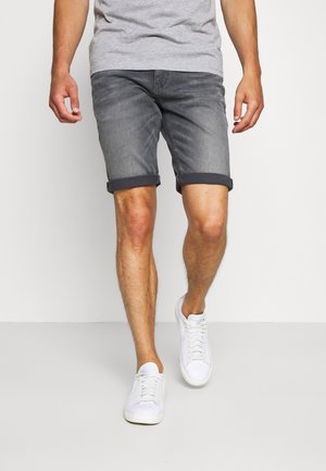 Szare szorty jeansowe z podwiniętymi mankietami, zestawione z białymi trampkami. Materiał wydaje się lekko przetarty, co dodaje tekstury i stylu.