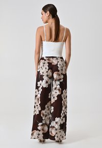 Witte spaghetti-top gecombineerd met wijde broek met een donkerbloemig patroon in beige en wit, van een gladde satijnen stof en enkel lengte.