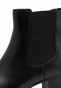 Bottine noire en cuir brillant avec un panneau élastique texturé sur le côté, dotée d'un talon bloc moyen et de détails de couture précis.