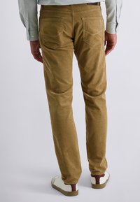 Khakifarbene Cord-Hosen mit Gesäßtaschen, tapered Fit, weiche Textur, kombiniert mit weißen Sneakers mit weinroten Akzenten.