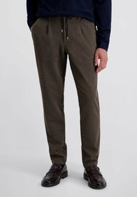 Bruine geklede broeken met een trekkoord in de taille en zijzakken, gecombineerd met donkere loafers en een marineblauw bovenstuk, met een ontspannen pasvorm.