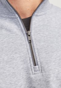 Sweatshirt léger gris clair avec une fermeture éclair d'un quart de longueur, présentant un tissu texturé et une couche intérieure noire contrastante.