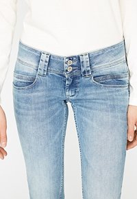 Ljusblå jeans i denim med tvåknappsstängning, fem fickor och subtila blekningar. Tyget har en slät textur med en klassisk passform.