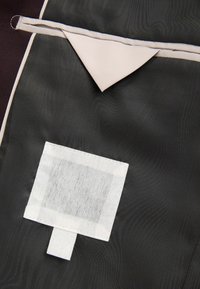 Czarny materiał o gładkiej fakturze z beżowym trójkątnym akcentem i białą prostokątną metką z uchwytem.
