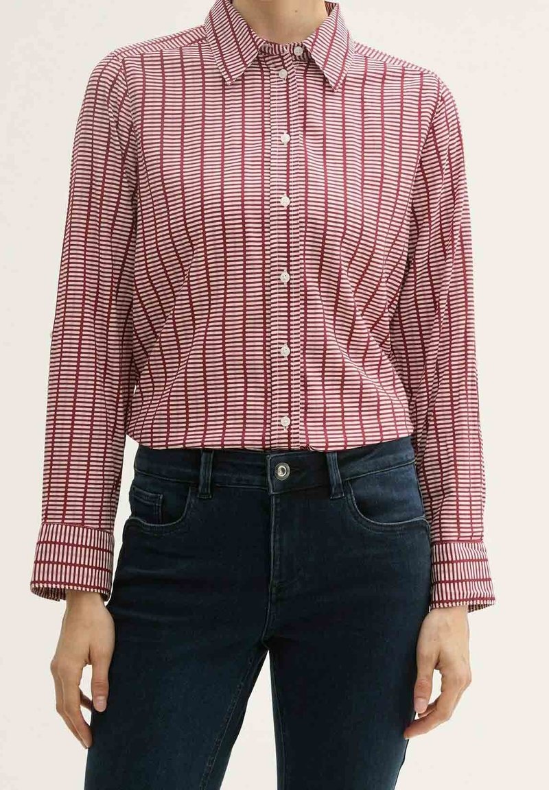Femme portant une chemise à manches longues boutonnée avec des rayures verticales rouges et blanches et un jean taille haute bleu foncé.