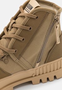 Stivali alla caviglia beige caratterizzati da una combinazione di tela texturizzata e pelle, lacci tondi color beige e una cerniera laterale per un facile accesso.