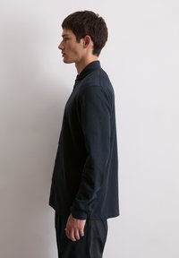 Camicia a maniche lunghe di un blu navy scuro con colletto, dotata di una chiusura con bottoni, texture morbida e vestibilità rilassata, abbinata a pantaloni neri.