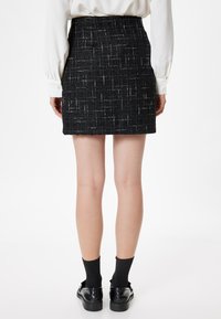 Sort tweed mini skørt med et struktureret m�ønster, flad talje og lige skæring; båret med sorte sko og strømper.