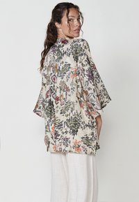 Kimono de lino con estampado floral y mangas tres cuartos, que presenta tonalidades de verde, naranja y púrpura sobre un fondo beige.
