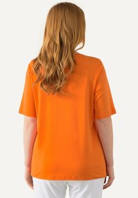 Maglietta arancione a maniche corte con una vestibilità rilassata. Realizzata in tessuto morbido, presenta un colletto rotondo e un orlo dritto. Nessun motivo visibile o accessori.