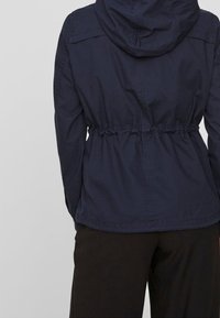 Navy hooded jacket with a drawstring waist, made of a lightweight fabric. Features a simple design with elastic hem and cuffs.