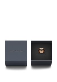 Ružovo-zlatý prsteň so tromi prepletenými pántmi v námorníckej darčekovej krabičke vystlanej čiernym zamatom. Krabička obsahuje nápis "DANIEL WELLINGTON" zlatou farbou.
