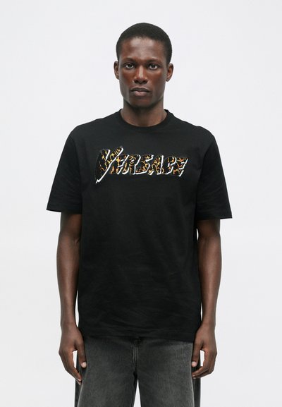 T-shirt de algodão preta com um ousado logotipo "Versace" texturado num vibrante padrão de estampado animal. Mangas curtas, design com decote redondo.