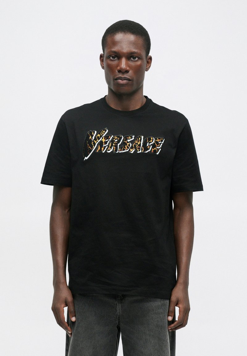 T-shirt en coton noir arborant un logo « Versace » audacieux et texturé, dans un motif coloré inspiré de la faune. Manches courtes et col rond.