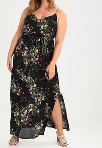 Musta maxi-mekko, jossa on pinkkejä ja purppuran värisiä kukkakuoseja, ohuet olkaimet, solmittava vyötärö ja korkea halkio yhdellä puolella.