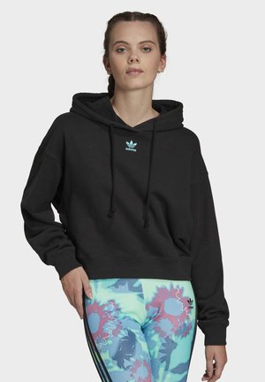 Fekete, cropped kapucnis pulóver húzózsinórral és világoskék Adidas logóval. Színes leggings-szel párosítva, amelyek virágmintákkal és csíkokkal díszítettek.