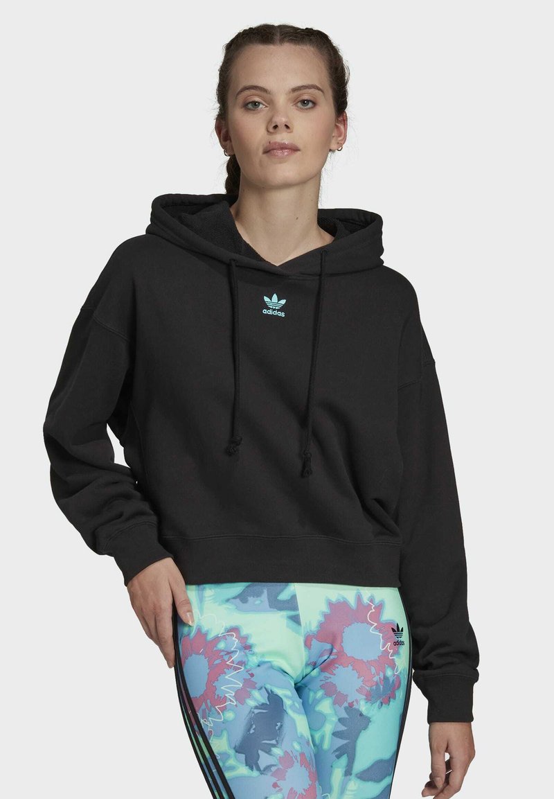 Svart kort hoodie med snörning och en ljusblå Adidas-logga. Matcher med färgglada leggings med blommönster och ränder.