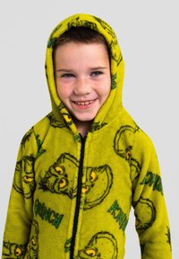 Felpa con cappuccio verde in pile con zip, caratterizzata da volti del Grinch in stile cartone animato e scritte, dotata di tasche a marsupio e finitura morbida e testurizzata.