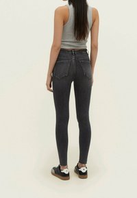 Tmavě šedé skinny jeans s vysokým pasem, jemně s opotřebením na kolenou a roztrhaným lemem, zkombinované s černými teniskami s bílými detaily.