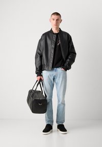 Schwarze Kunstleder-Bomberjacke, schwarzes T-Shirt, hellblaue Jeans, schwarze Sporttasche und schwarze Sneaker mit weißen Sohlen. Minimalistisches Design.