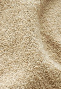 Beige textiel met een zachte, iets pluizige oppervlakte, gekenmerkt door gelijkmatig verdeelde lussen en een warme, neutrale kleur.