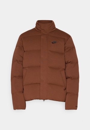 Chaqueta puffer marrón con un alto cuello, que cuenta con cierre de cremallera, diseño acolchado horizontal y un logo negro de Nike en el pecho.