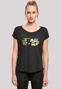 Svart T-skjorte med korte ermer og rund hals, som har et flerfarget "STAR WARS" grafisk design på forsiden. Myk tekstur.