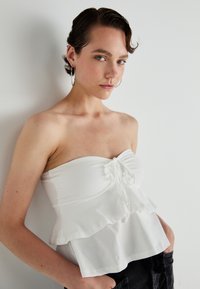 Witte strapless top met een verzamelde voorkant en een gerimpelde onderkant, gemaakt van een gladde stof; heeft een trekkoord detail bij de buste.