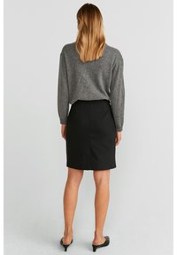 Pull en tricot gris à manches longues, associé à une jupe crayon noire, vu de dos. Tissu lisse et design minimaliste.