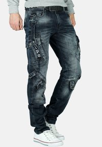Pantalons cargo en denim bleu foncé avec des coutures contrastées, de multiples poches et une coupe slim. Associés à des baskets blanches.