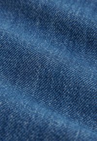 Gros plan sur un tissu de denim bleu texturé montrant le tissage détaillé et de légers plis.