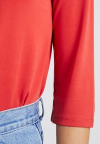 Rode top met driekwart mouwen van een gladde stof, gecombineerd met hoge blauwe denim shorts met een aangesloten tailleband.