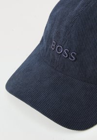 Mørkeblå kordfløjlskasket med buet skygge og broderet "BOSS" logo i matchende farve, med struktureret design og struktureret stof.