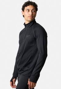 Zwarte sportieve pullover met hoge kraag, half-rits aan de voorkant, textuurpanelen en duimgaten in de mouwen. Heeft een subtiele logo op de borst.