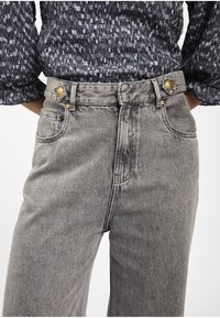 Grijze denim jeans met een hoge taille, voorzien van hardware in goudkleur bij de tailleband en twee voorzakken. De textuur is glad.