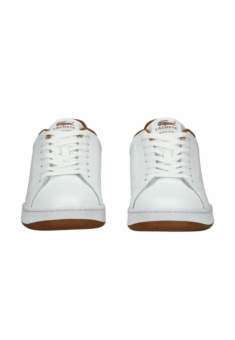 Baskets blanches à lacets avec tige en cuir, bout rond et semelle en caoutchouc présentant des accents marron. Logo visible sur la languette.