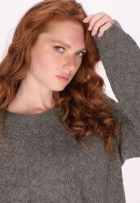 Szürke kötött pulóver, texturált gyémántmintával, kerek nyakkivágással és laza szabással. Hosszú ujjai és puha anyaga otthonos megjelenést kölcsönöz.