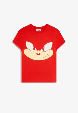 Červené tričko s krátkými rukávy s velkou stylizovanou podobou tváře Sonic the Hedgehog s odhodlanýma očima a úsměvem na přední straně.